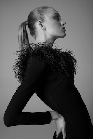 Mulher elegante em vestido preto com detalhes de penas nos ombros.