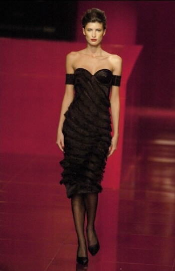 Modelo de vestido preto desfilando em uma passarela.